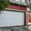 White garage door on gravel driveway with snow, red siding home in winter