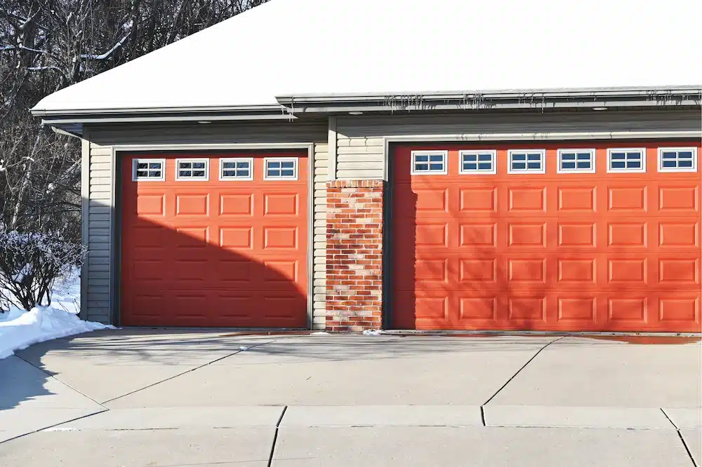Orange garage doors with icicles on the eaves and snow melting on driveway