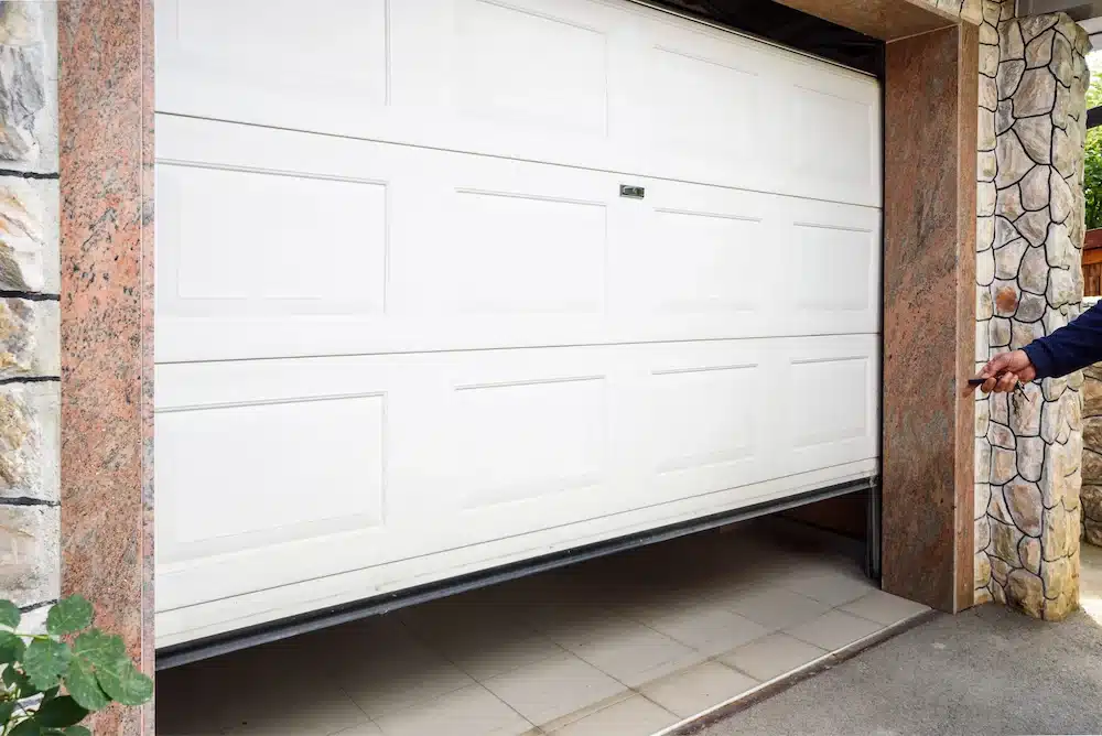Garage door partially open with a remote opener held in hand